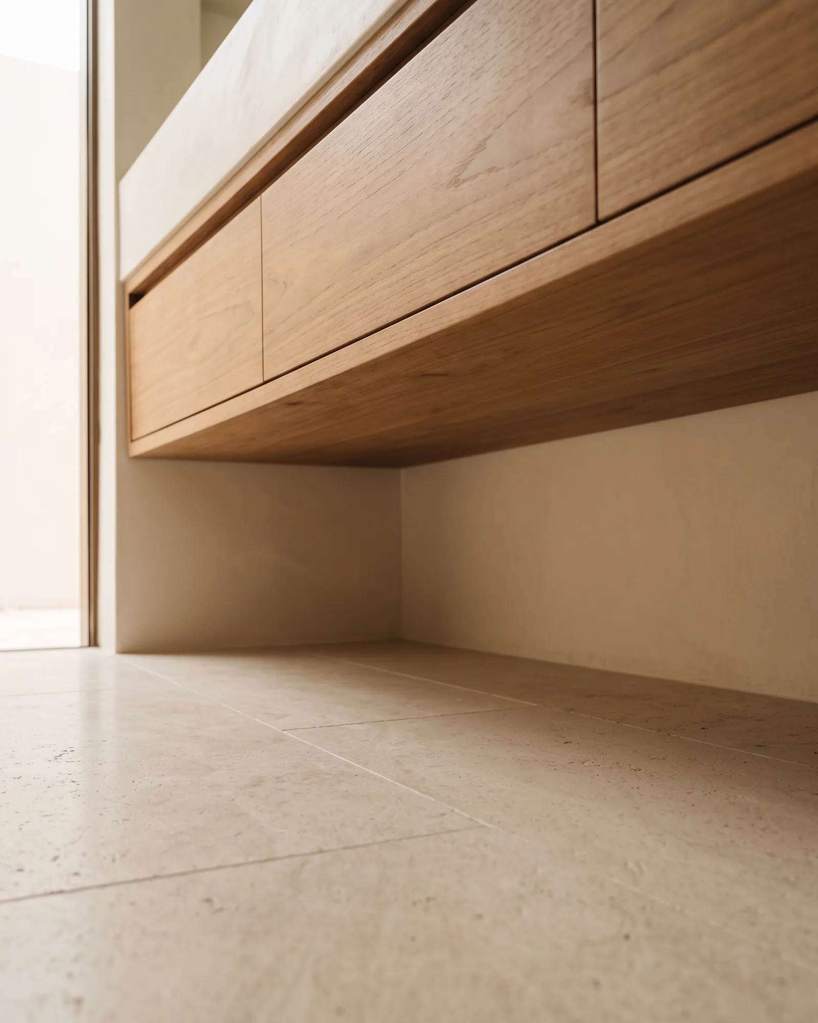 A floor-level view under a wall-hung vanity, showing its sealed underside and a clear air gap above dry tiled floor.