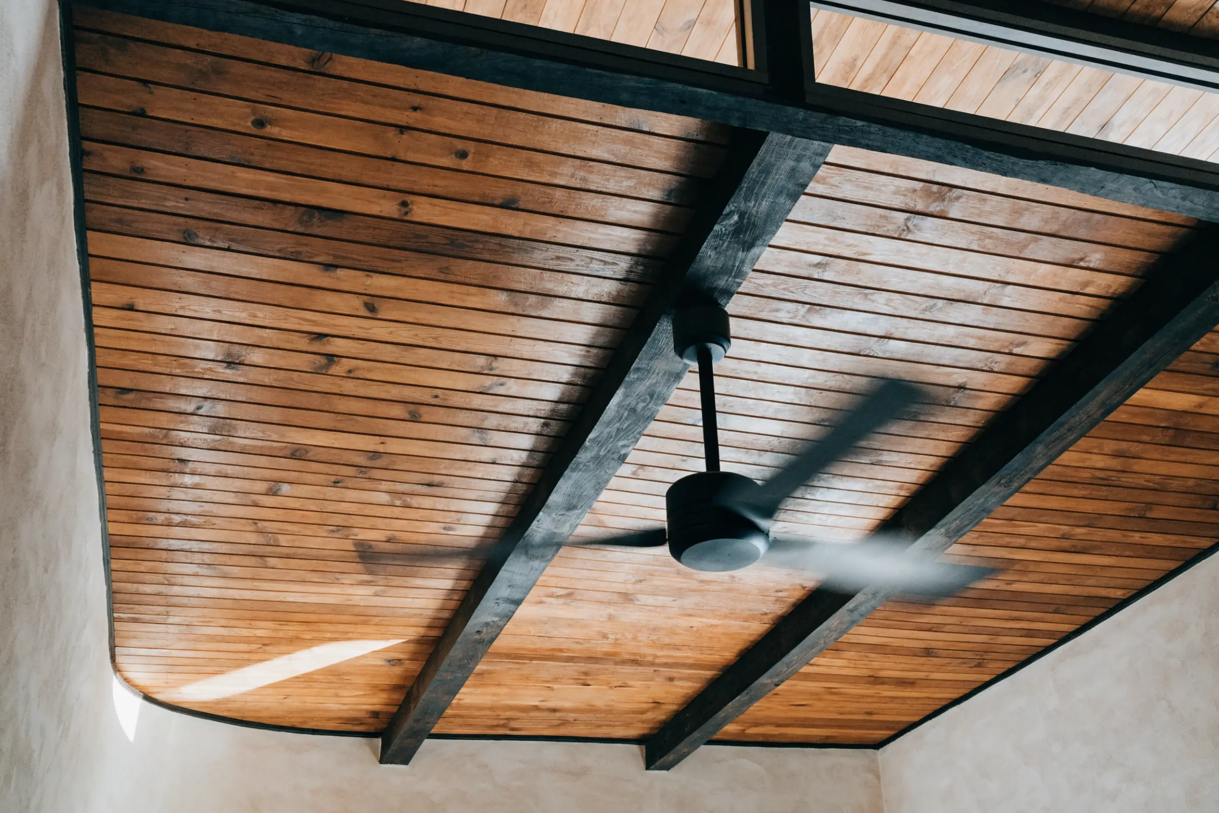 Plank wood ceiling with dark beams and a ceiling fan, its blades softly blurred with motion