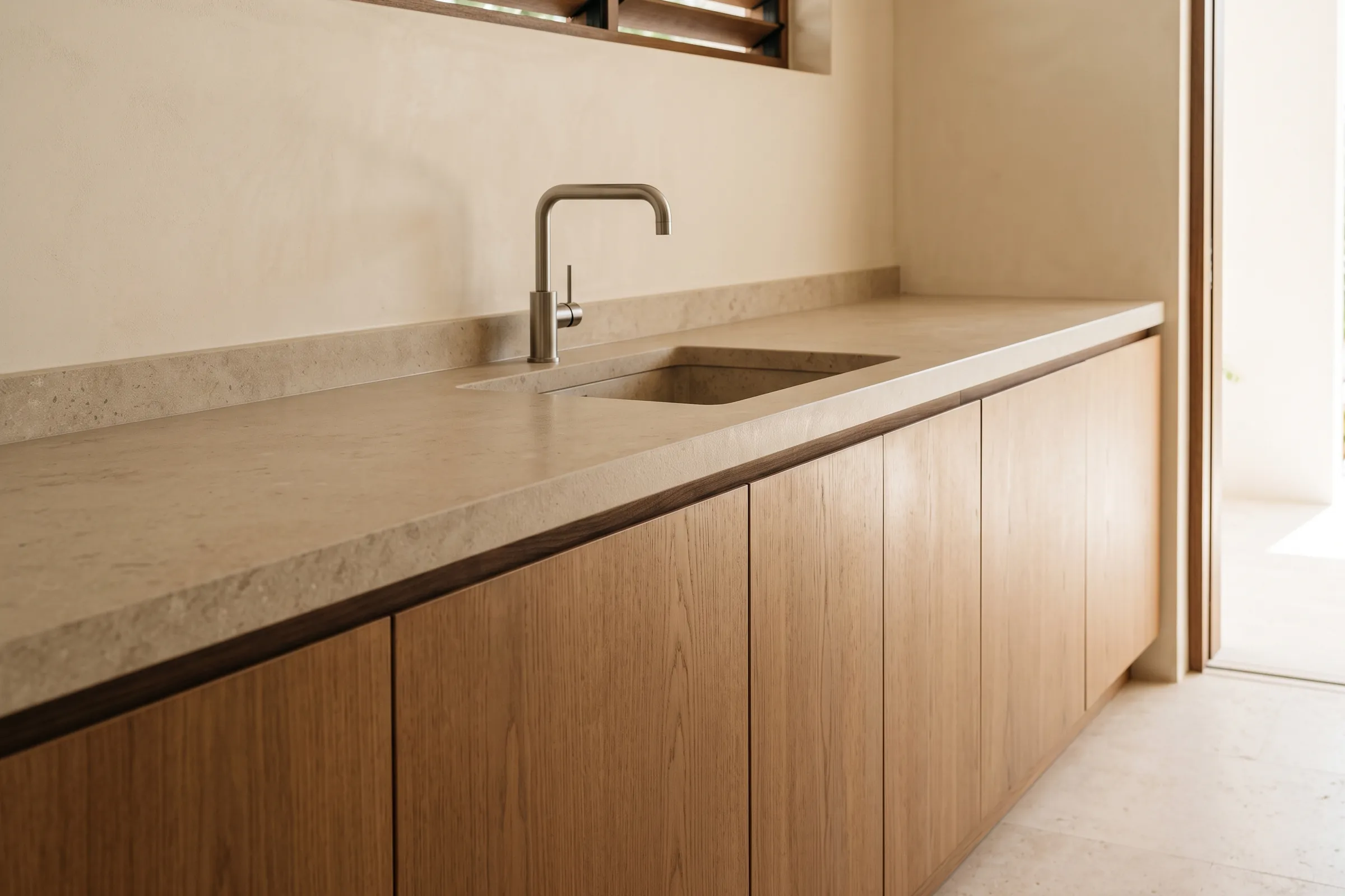 A pale stone worktop running the length of a kitchen, with an integrated basin and tap above a row of oak cabinet fronts.
