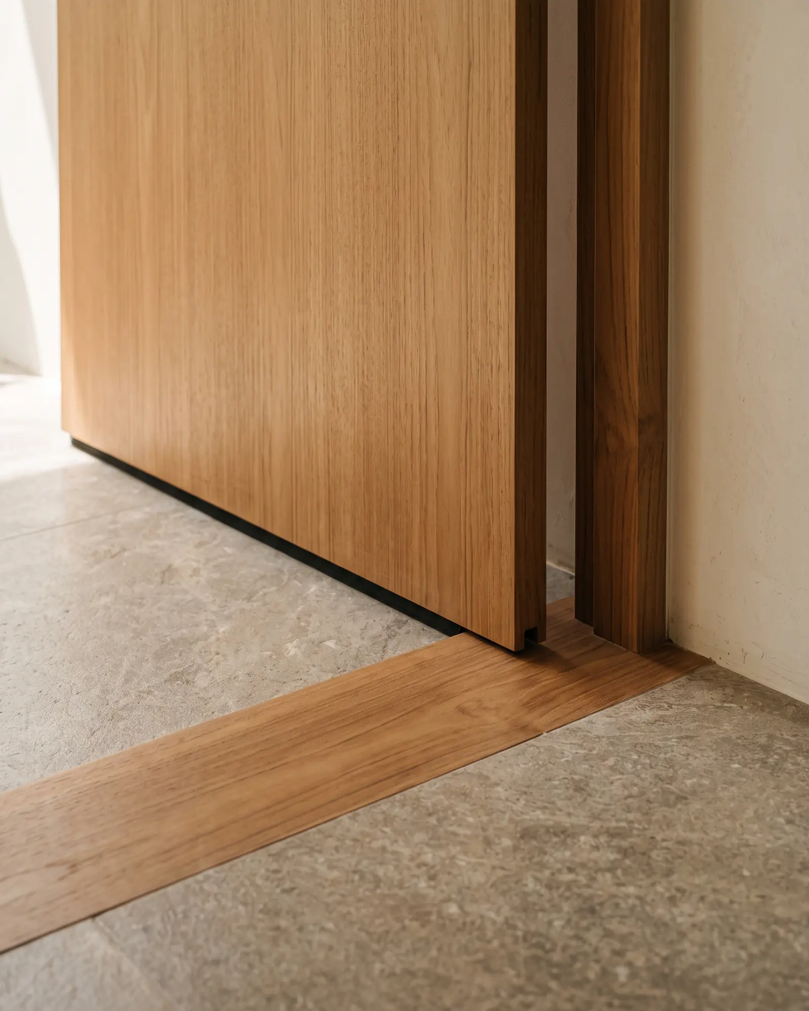 The foot of a door leaf meeting the frame leg, with a timber threshold strip running across the opening and a shadow gap under the leaf.