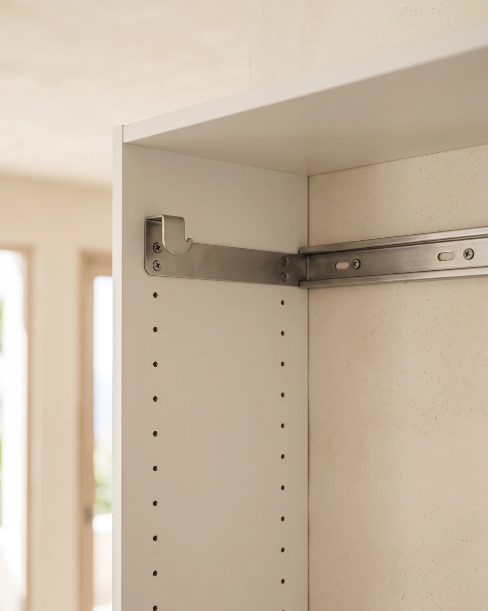 A cabinet bracket hooked over a steel wall rail inside a white carcass, with rows of shelf-pin holes running down the side panel.