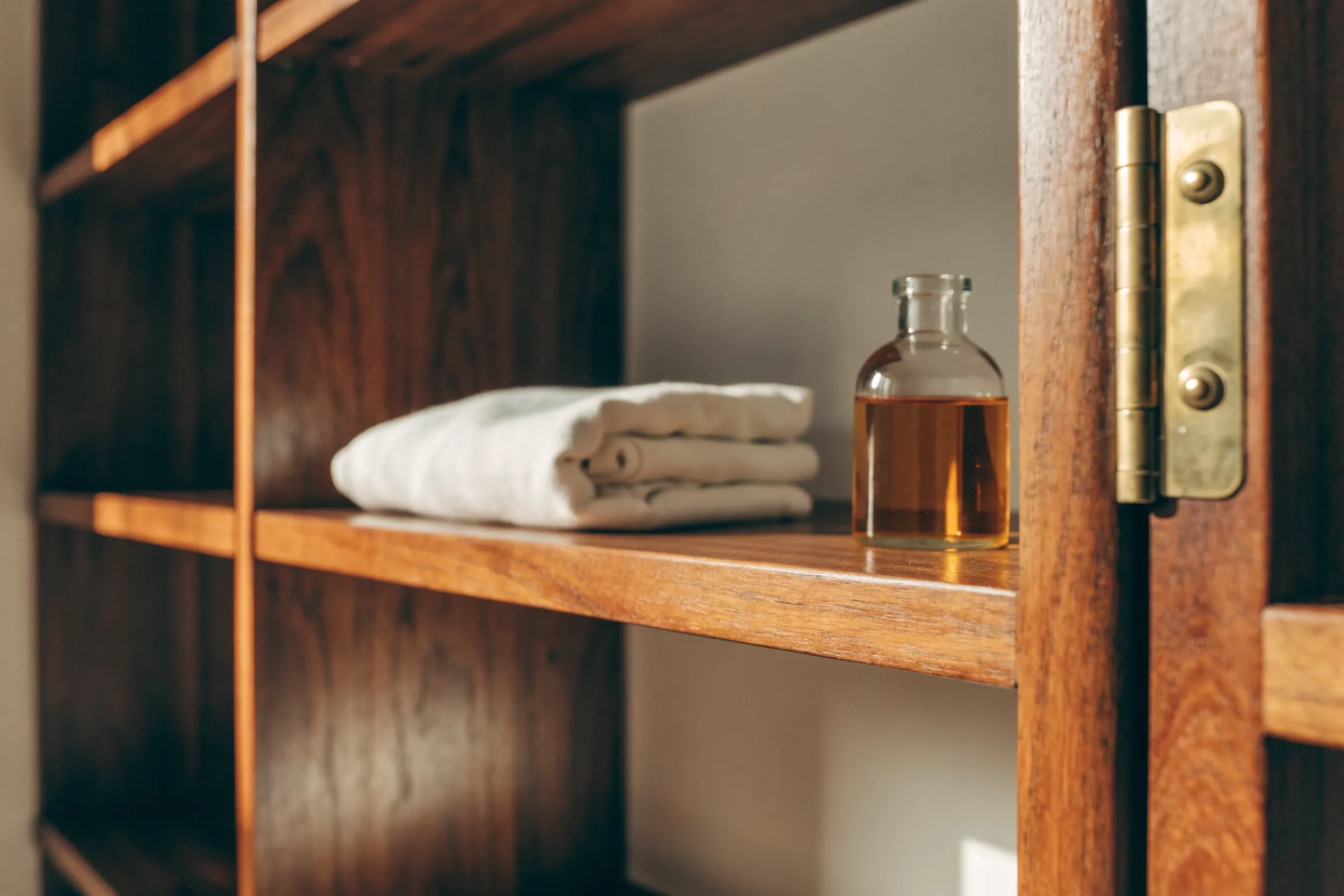 Folded cleaning cloth and a small bottle of furniture oil on a teak shelf beside a brass hinge