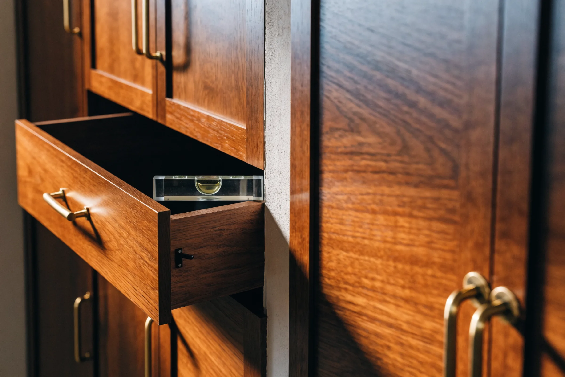 Spirit level resting on an open drawer box below cabinet doors with even gaps and brass handles