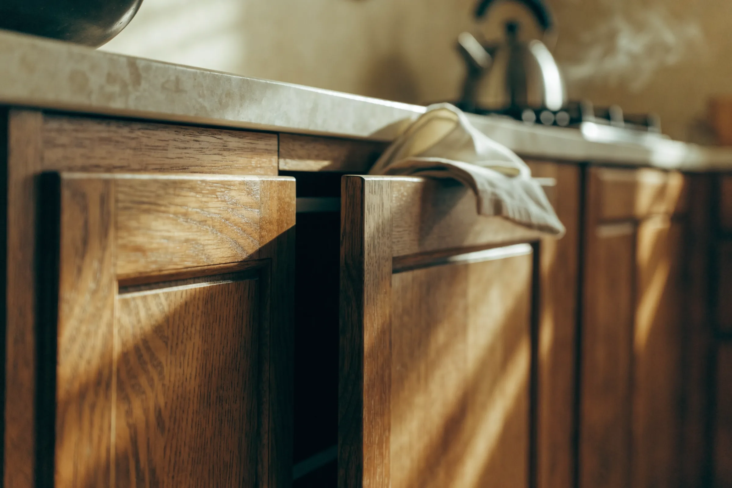 Wooden cabinet doors under a stone worktop, a cloth resting on one door edge and a kettle steaming behind