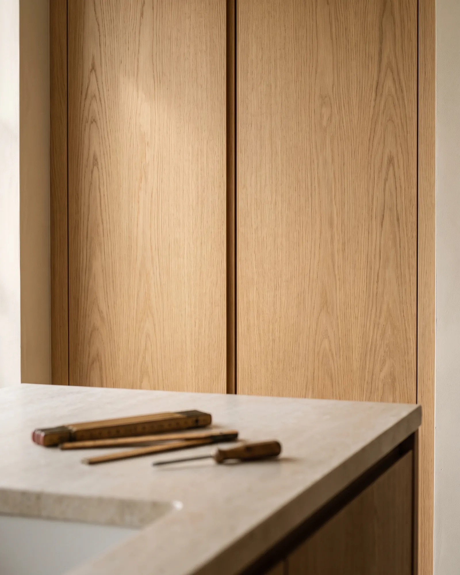 Even door gap on oak kitchen cabinets, a folding rule and screwdriver resting on the stone worktop