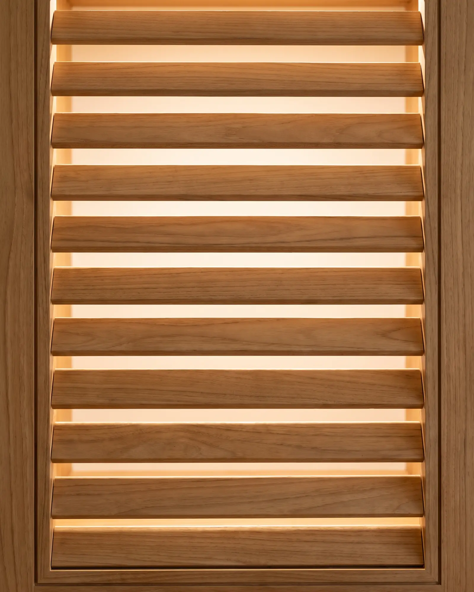 Close view of a louvred wardrobe door with eleven wide timber vanes, warm light glowing through the gap under each vane.