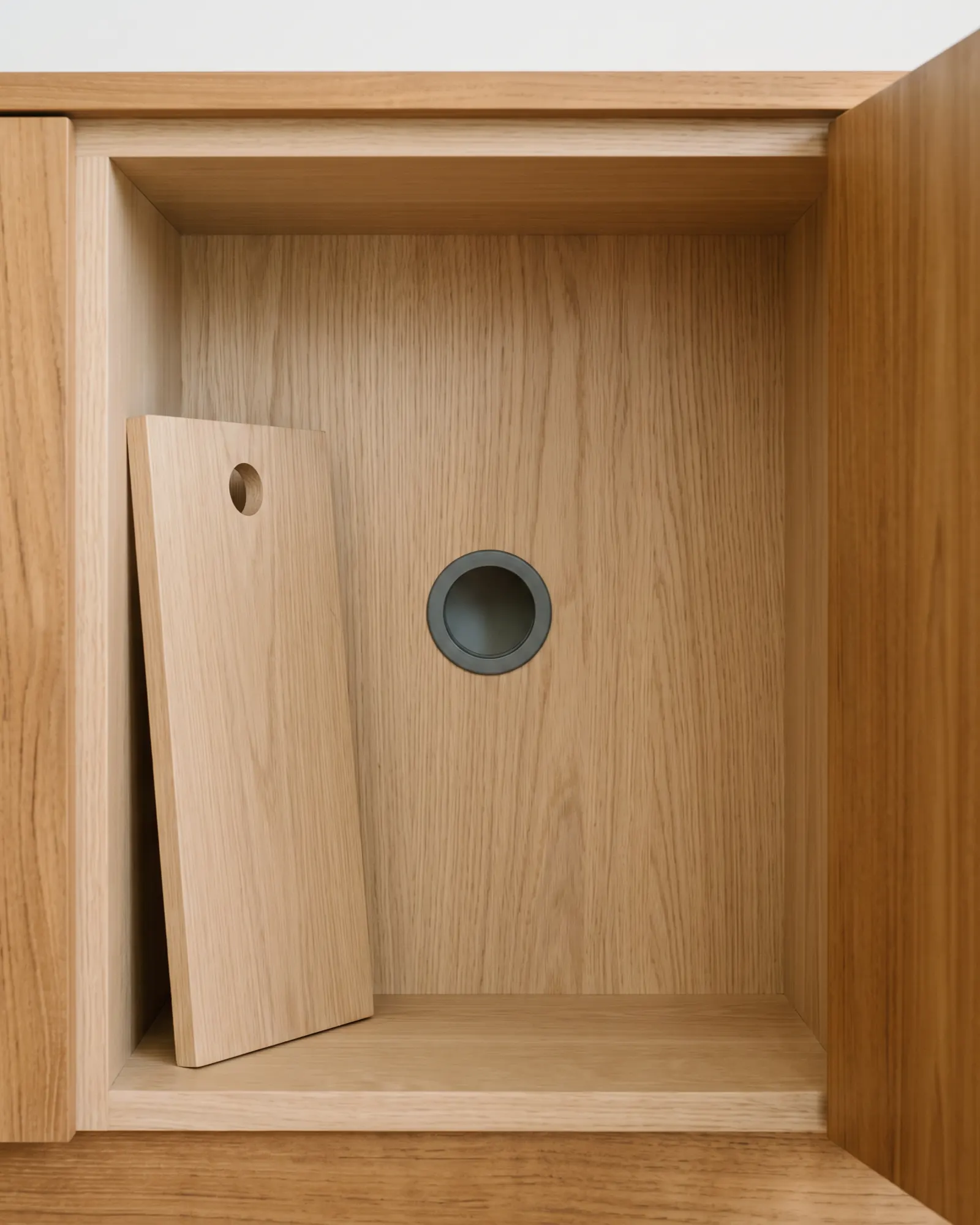 Open bay of an oak-lined media cabinet with a removable access panel standing upright inside it and a single flush dark cable grommet in the back panel.