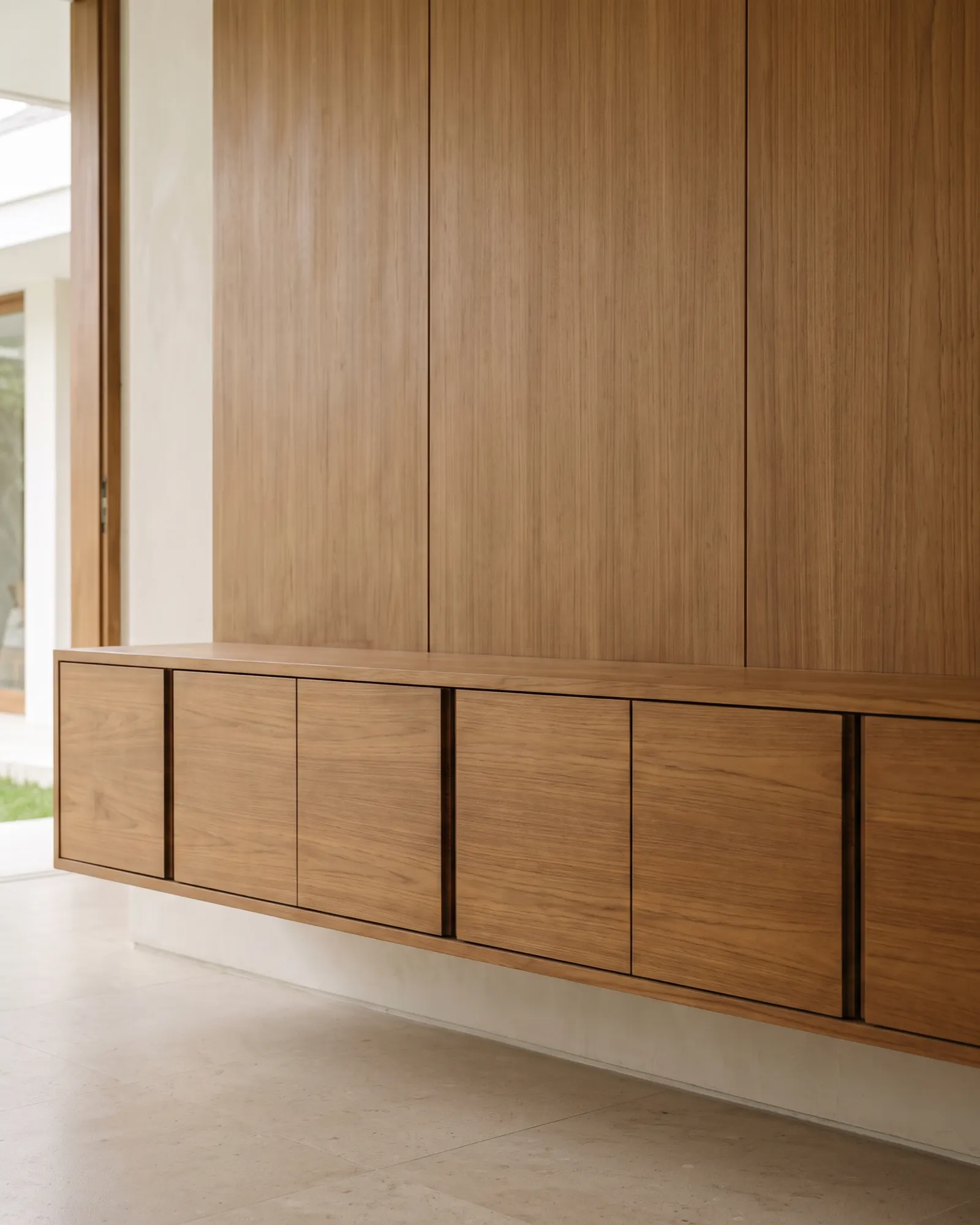 Floating handleless teak media cabinet beneath flush teak wall panelling, with clear shadow beneath the cabinet showing it carries no legs.