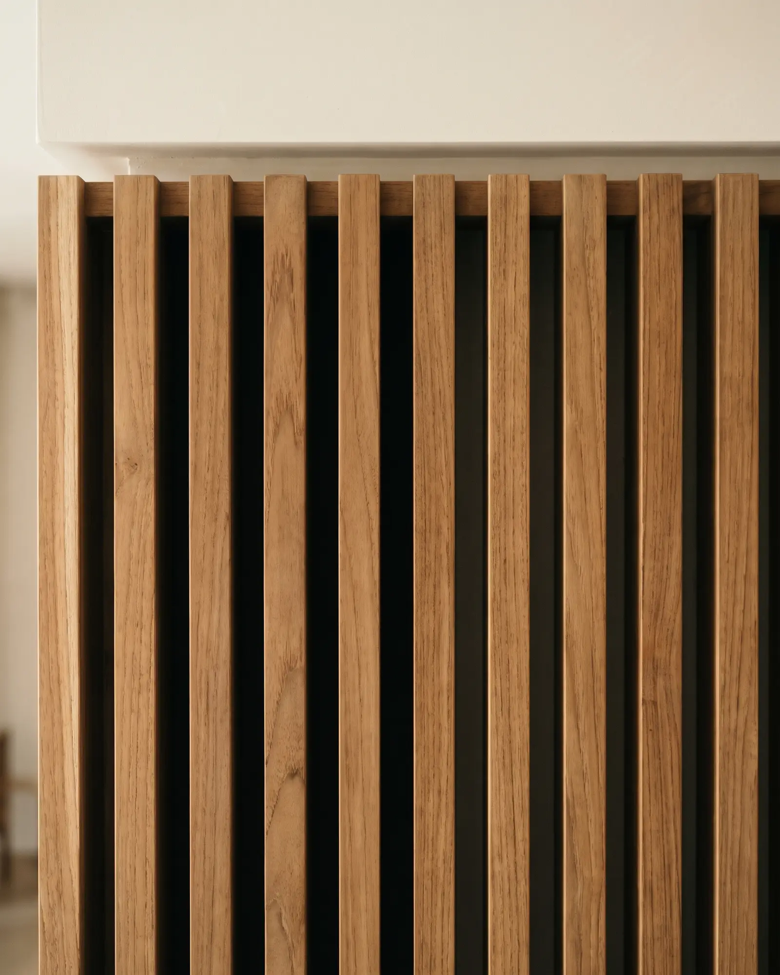 Close view of evenly spaced vertical teak slats stopping in a straight line under a narrow shadow gap at the ceiling.