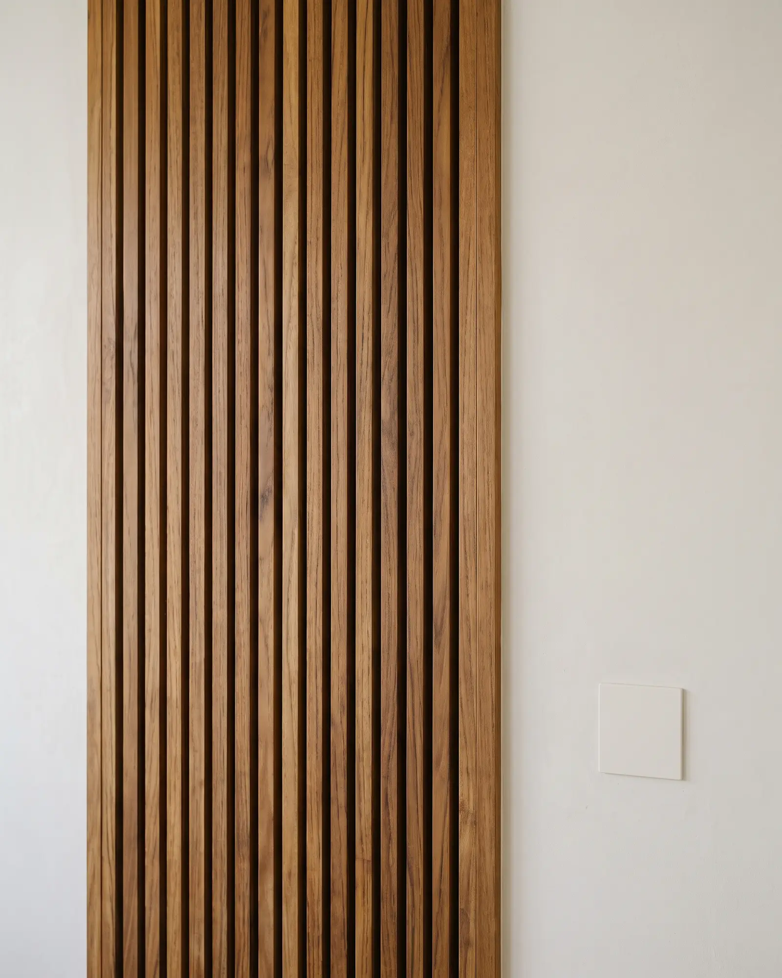 Vertical teak slat wall ending in a clean edge trim against a rendered wall, with a single blank flush socket plate set in the render beside it.