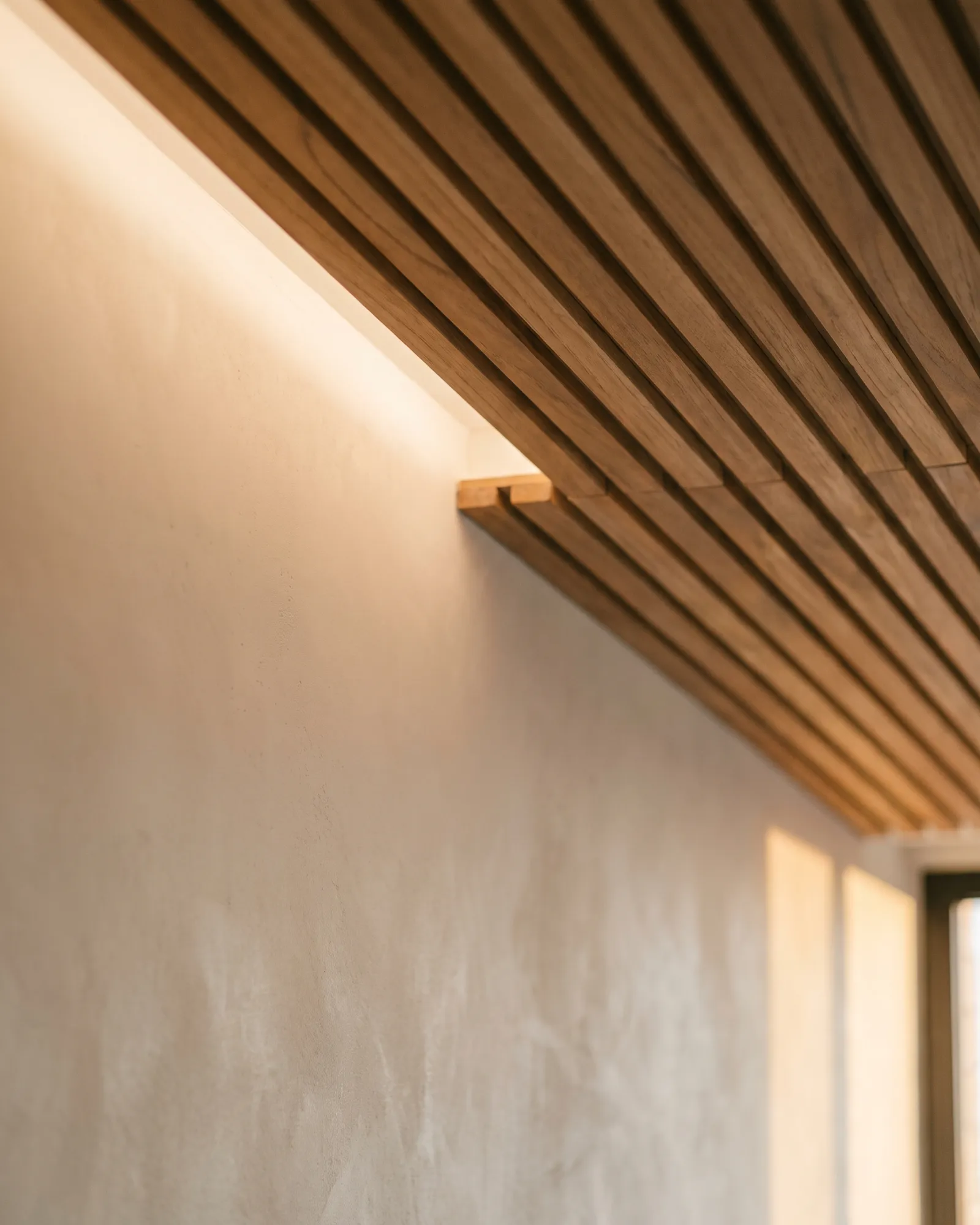 Slatted teak ceiling meeting a plaster wall above a concealed cove light