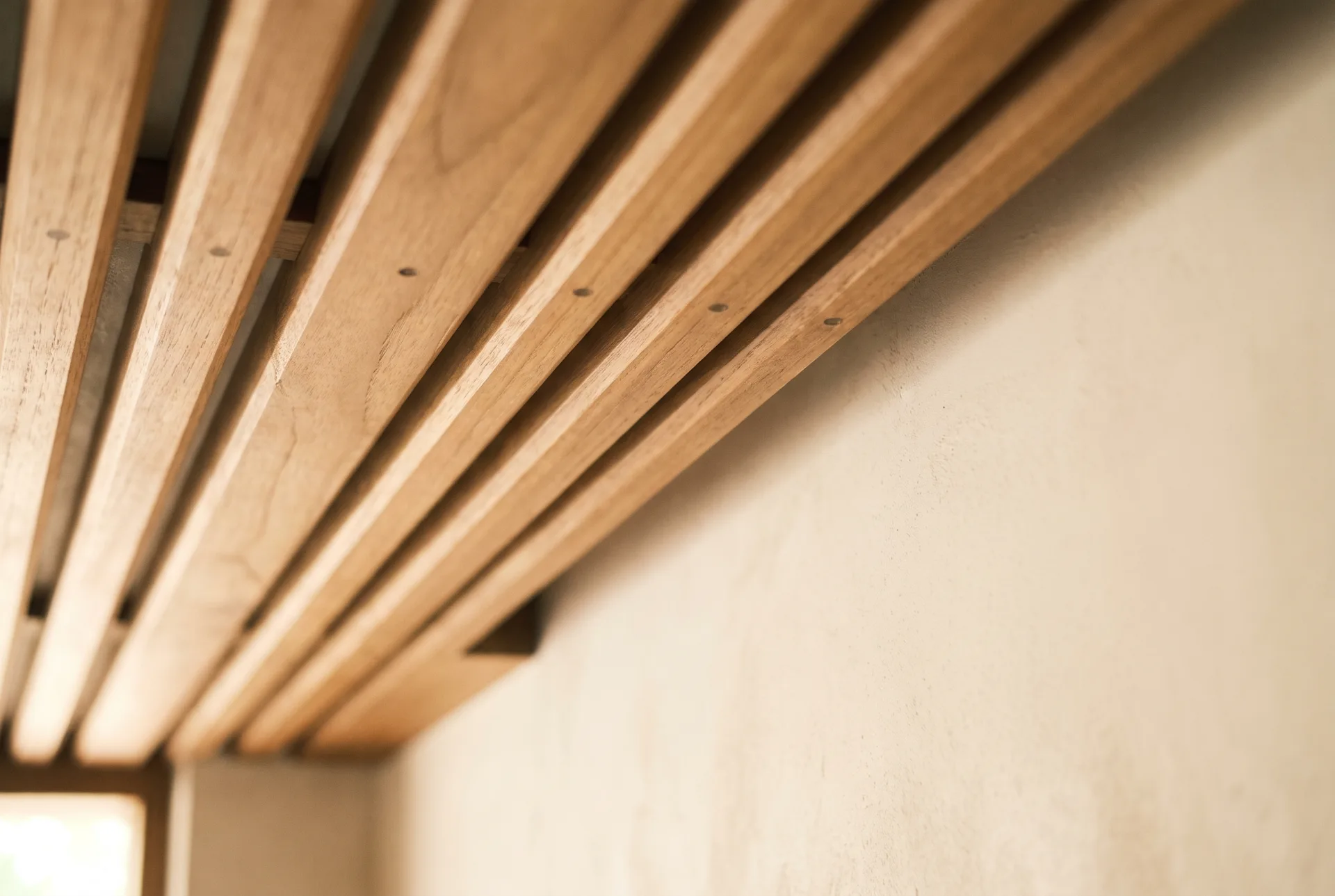 Close-up of teak ceiling battens meeting a plaster wall with even spacing