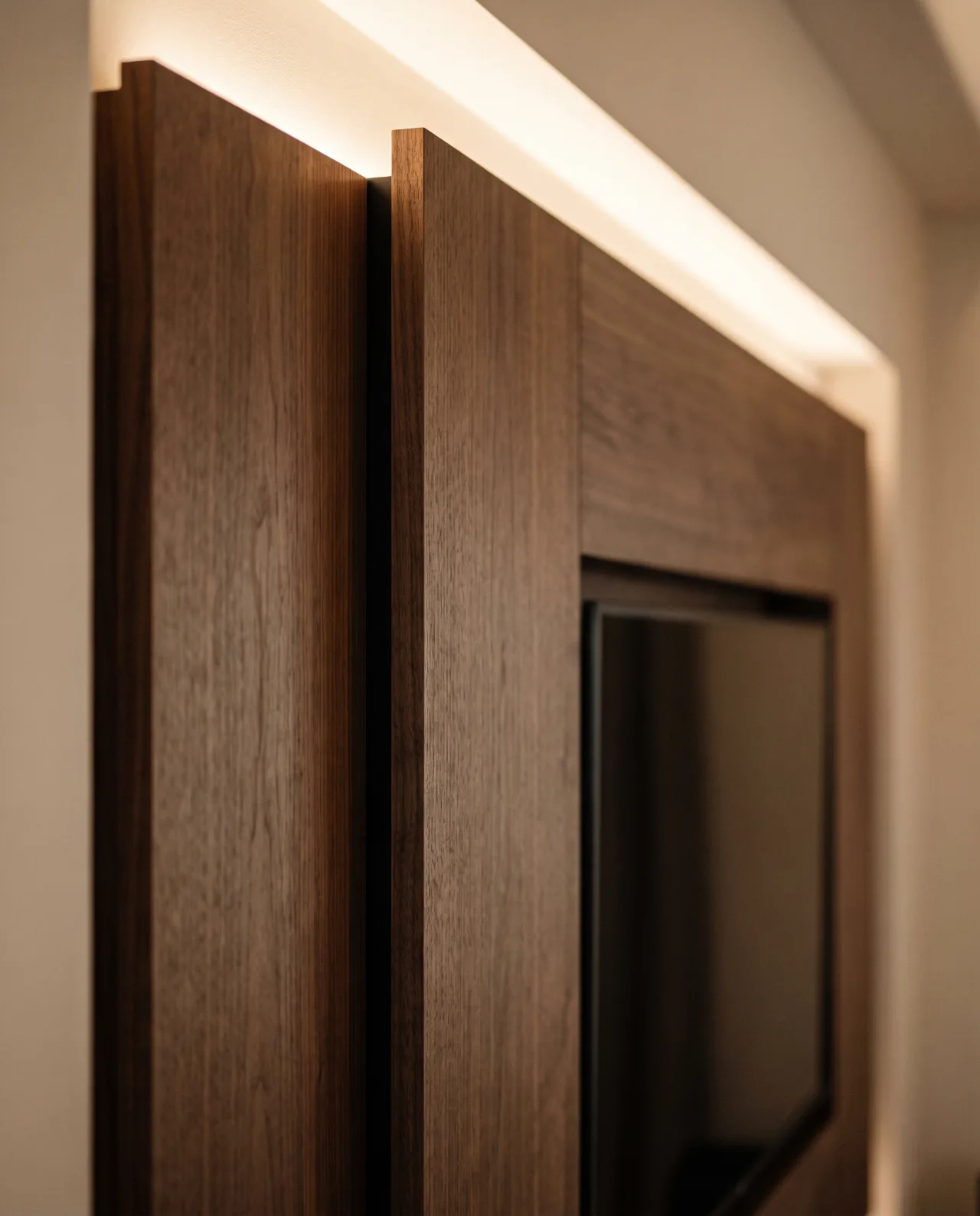 Close-up of walnut wall panels meeting in a precise joint under cove lighting