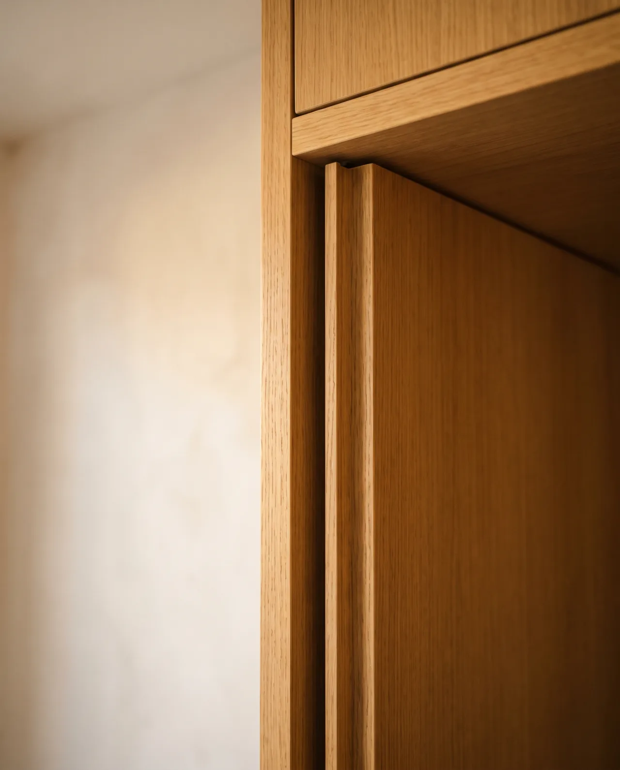 Close-up of a wardrobe door edge with milled pull groove and oak veneer finish