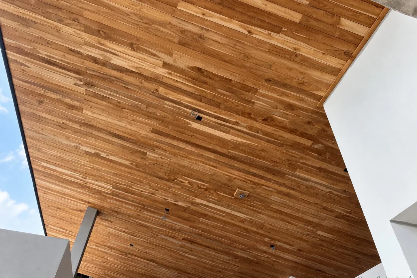 A finished teak board soffit following an angled roofline, seen from below against the sky