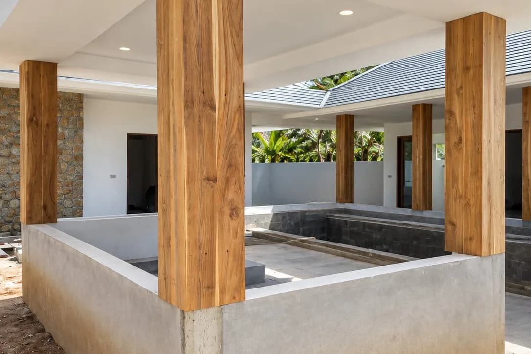 Teak-clad columns carrying a sala roof over a pool terrace during construction