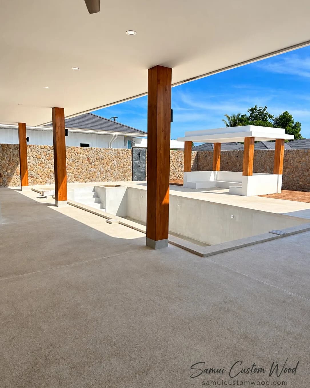 Teak-clad columns under a covered terrace beside a pool under construction