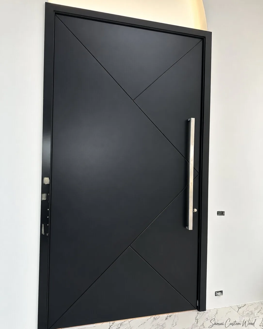 Matte black geometric-panel pivot door with a long steel pull