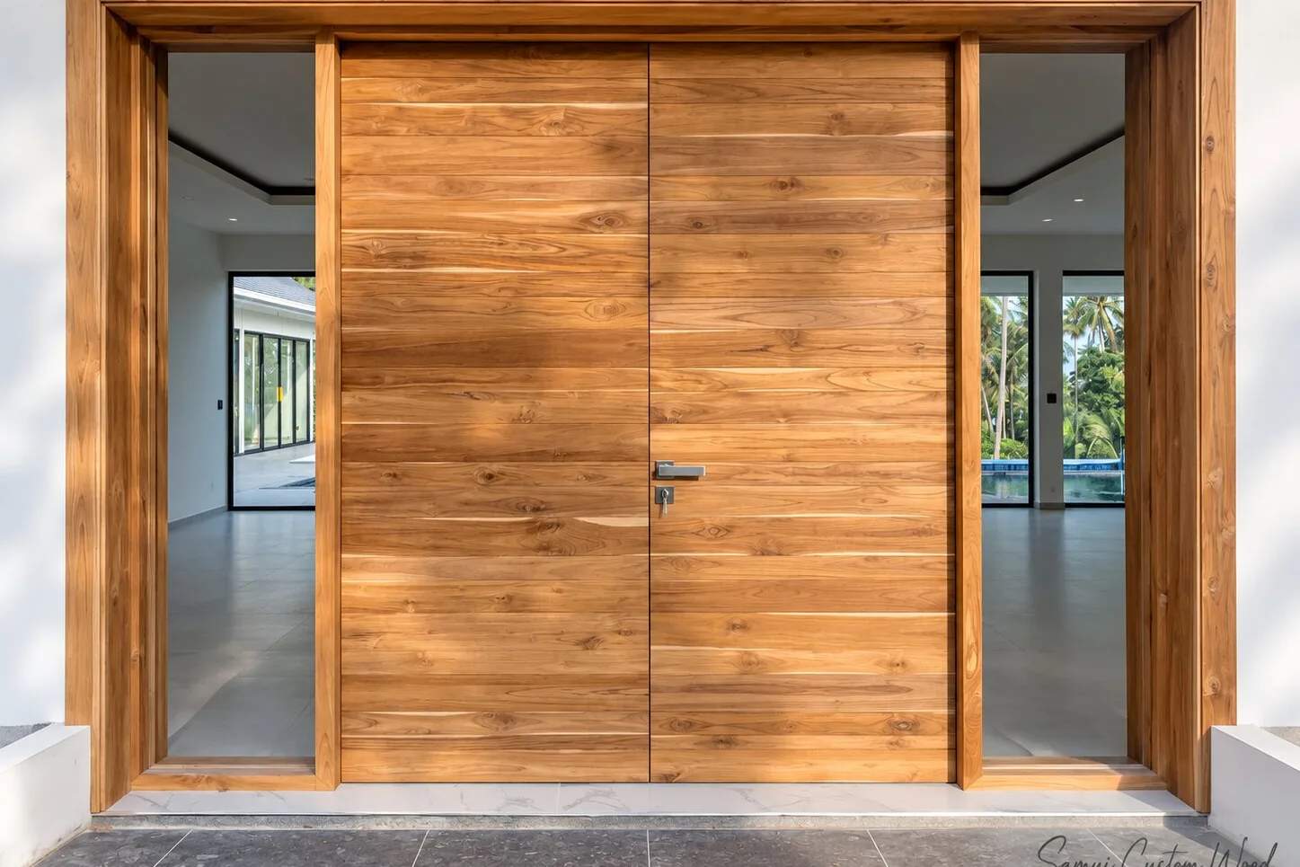 Wide teak sliding double doors closed across a villa entrance in a teak surround