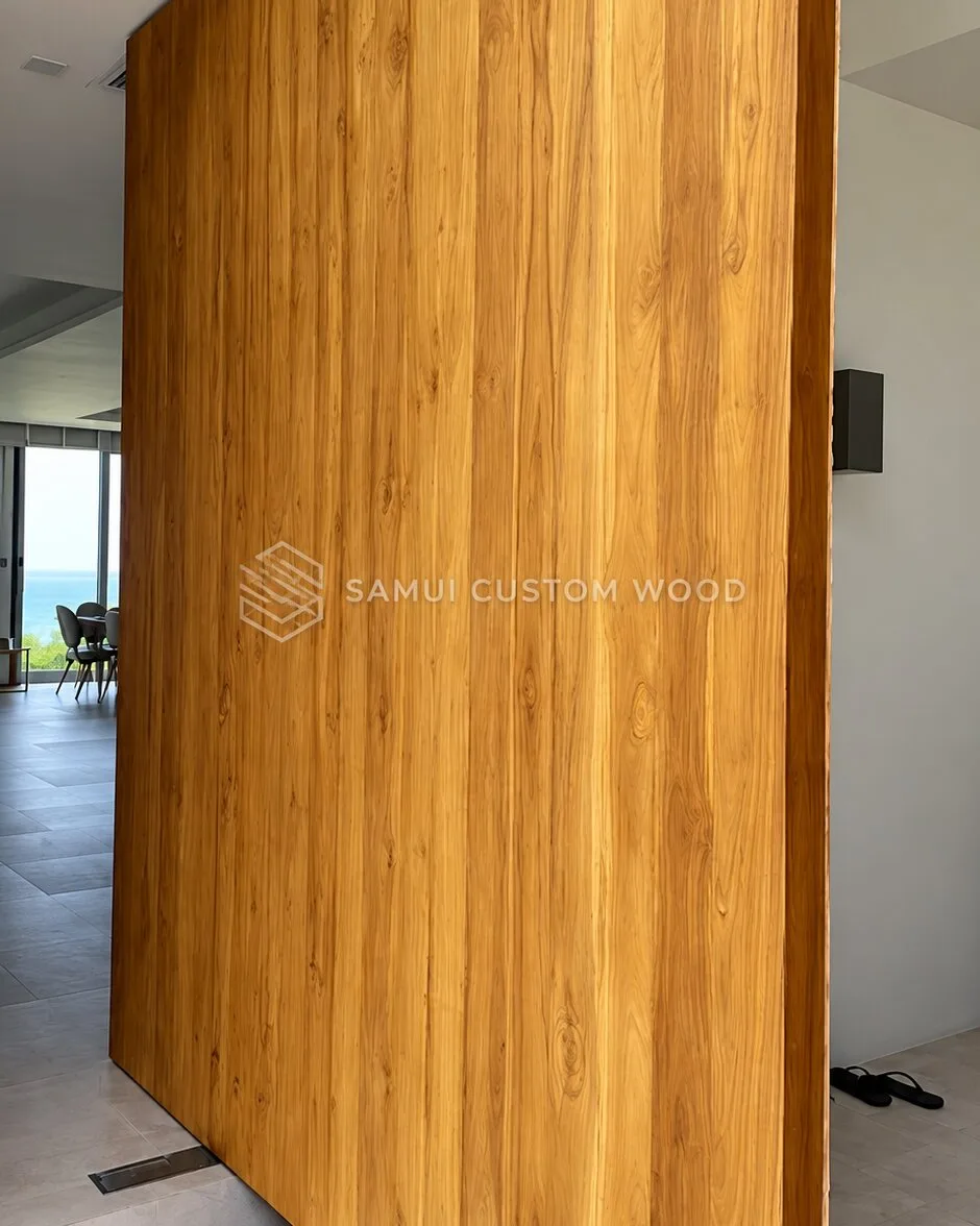 Full-height teak pivot entrance leaf standing open inside a bright hallway