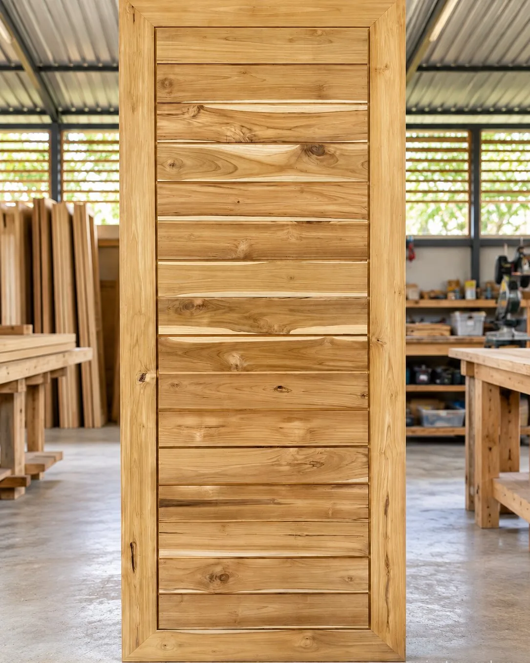 Slatted teak door standing upright in the workshop before delivery