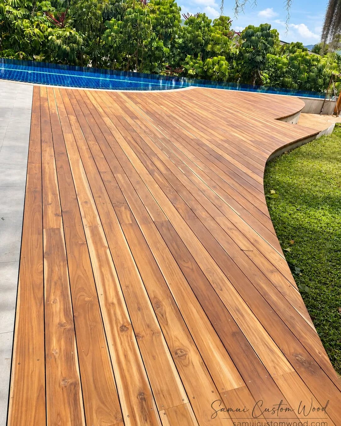 Curved teak pool deck sweeping between the water and a lawn
