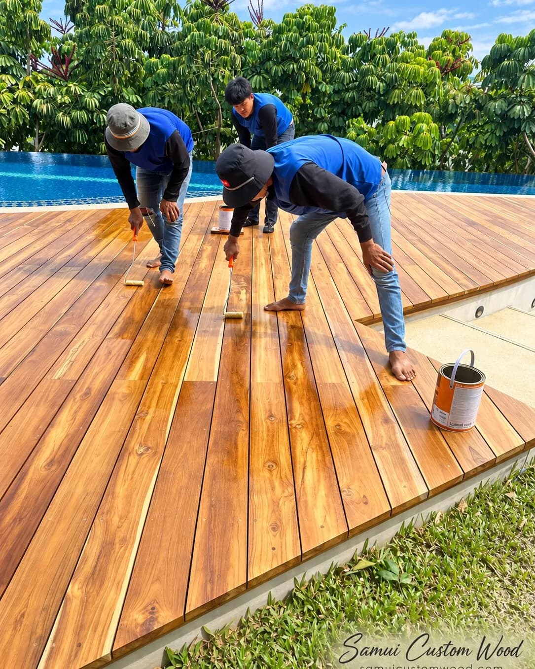 Three carpenters rolling oil onto fresh teak decking by an infinity pool