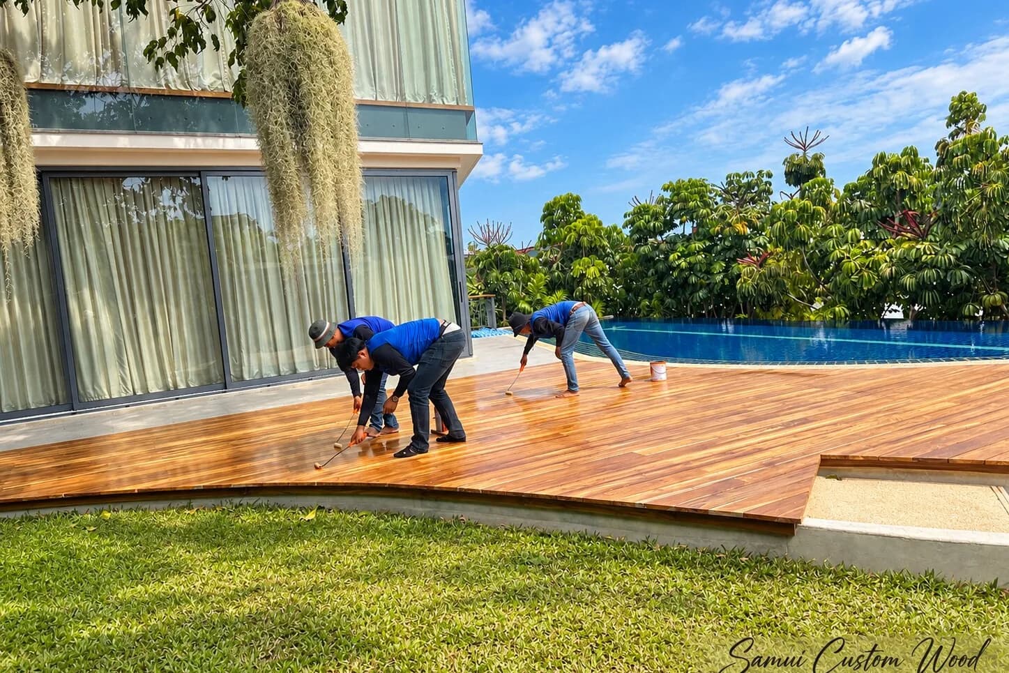 Crew oiling a poolside garden deck beside a villa facade