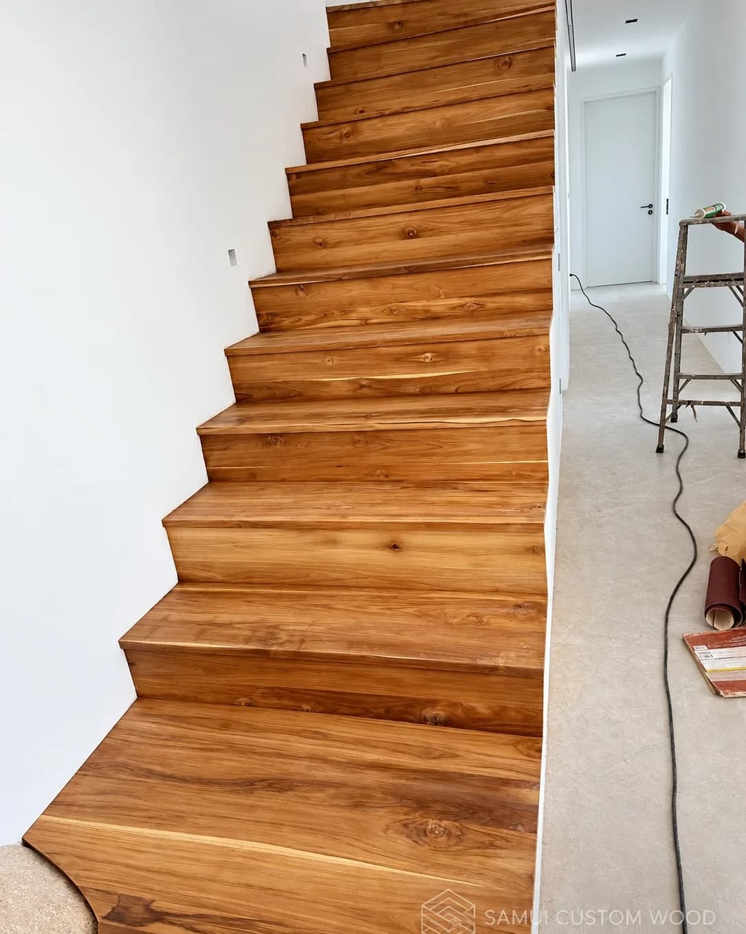 Side view of teak stair treads and risers during fitting, hallway beyond