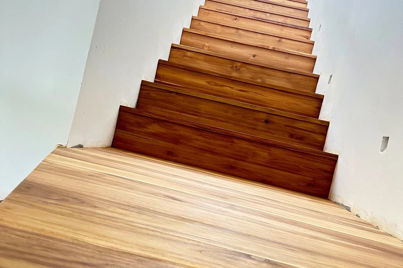 Solid teak staircase climbing between white walls, seen from the teak floor below