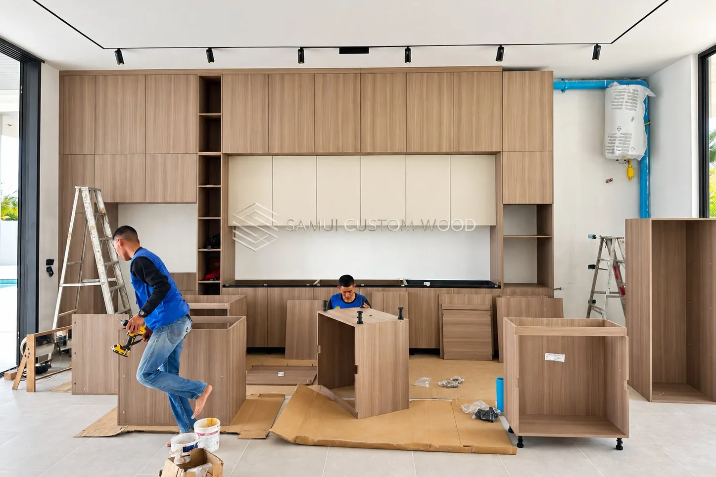Two carpenters assembling kitchen carcasses on a tiled floor beneath fitted wall units