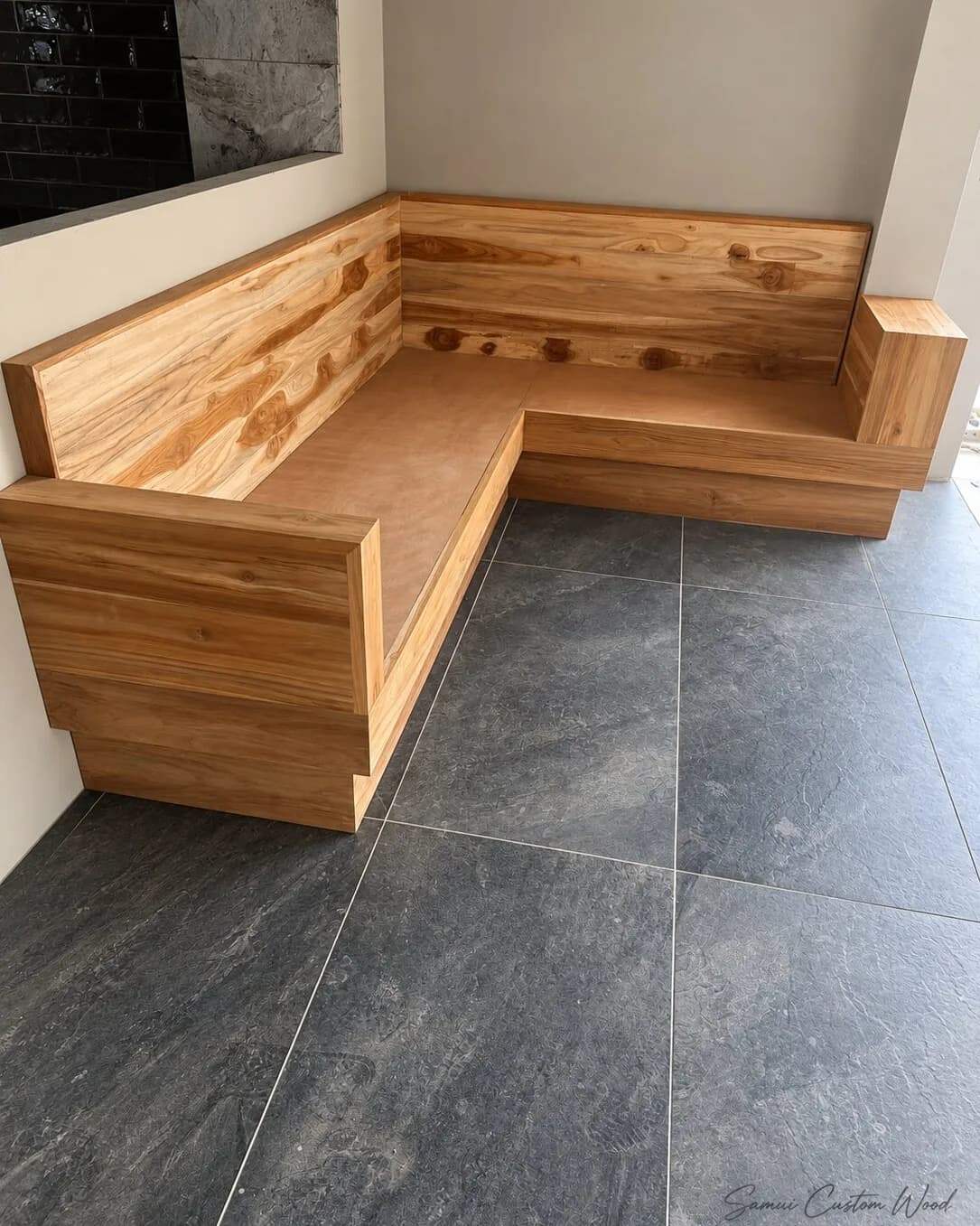 Built-in L-shaped timber bench seat in a corner on dark stone tiles