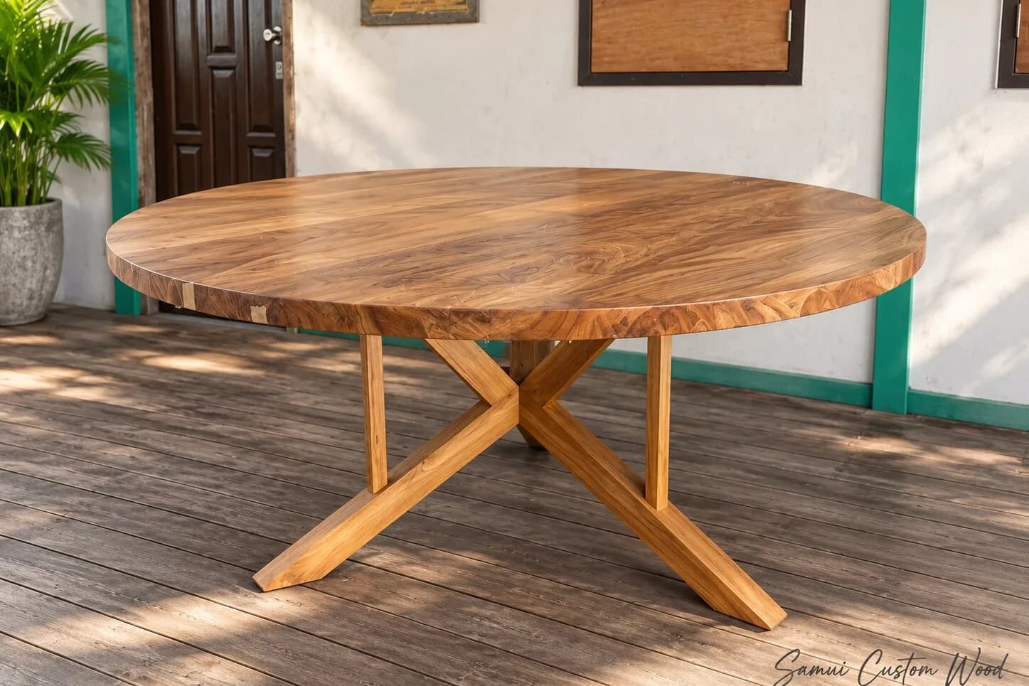 Round solid teak dining table with a sculptural cross base on a workshop deck