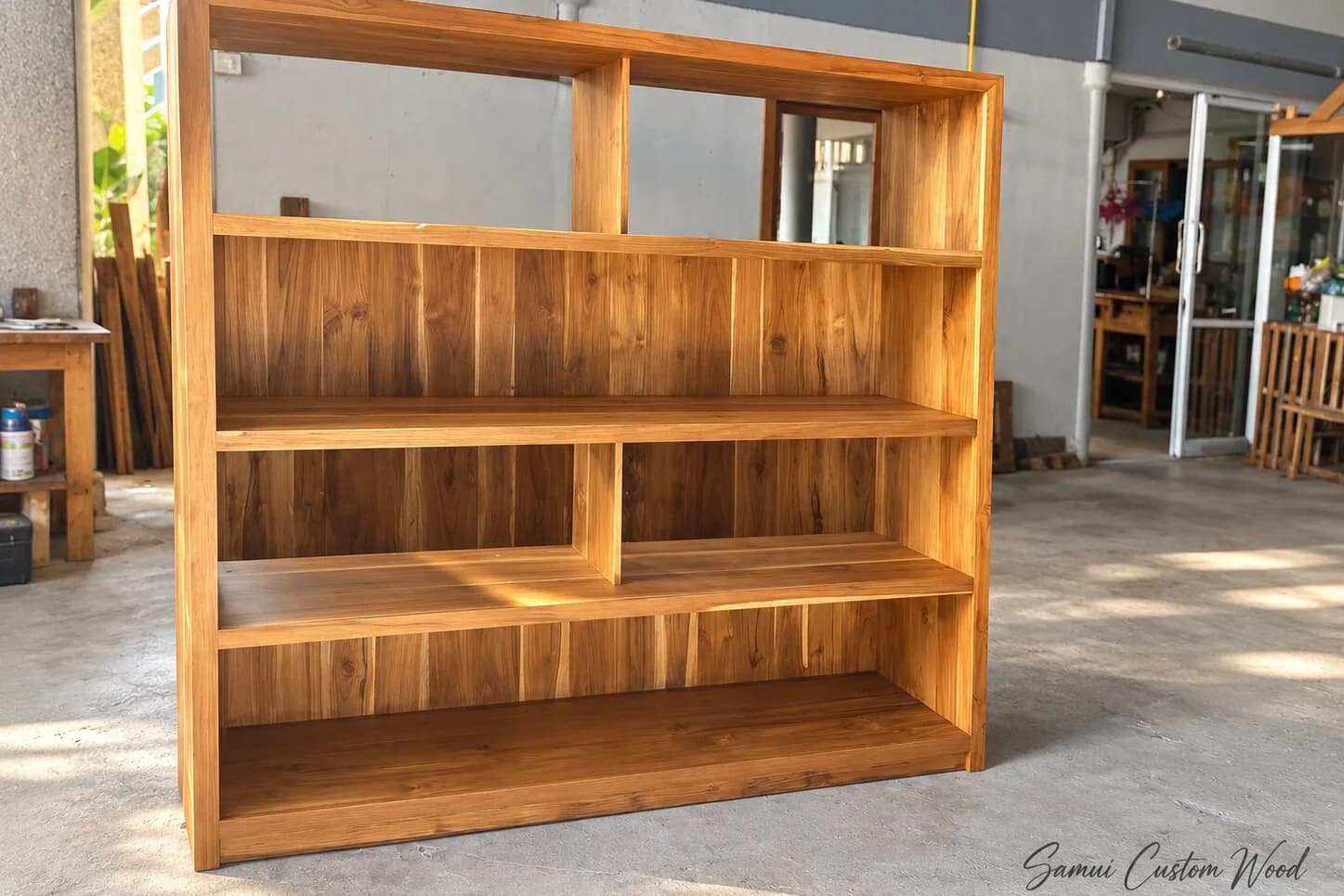 Freestanding teak bookcase with staggered shelves outside the workshop